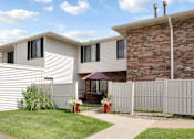 Thumbnail 18 of 36 - A house with a white fence and a patio with a table and chairs.