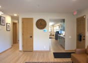 Thumbnail 23 of 27 - A hallway with a clock on the wall and a couch on the right side.