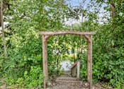 Thumbnail 44 of 67 - A wooden archway covered in greenery leads to a path.