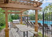 Thumbnail 47 of 67 - A wooden pergola with a grill and picnic table is situated next to a pool.