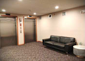 Thumbnail 70 of 78 - A black leather couch sits in a room with a carpeted floor and two elevators.