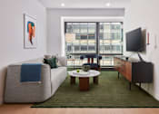 Thumbnail 10 of 15 - A living room with a grey couch, a coffee table, a flat screen TV and a window overlooking a city.