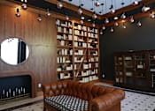 Thumbnail 5 of 32 - A brown leather couch sits in front of a bookshelf in a room with wooden walls.