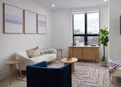Thumbnail 1 of 15 - A living room with a white couch, a blue chair, a wooden cabinet, and a flat screen TV mounted on the wall.