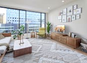 Thumbnail 18 of 42 - A living room with a large window, a white sofa, a wooden coffee table, and a rug with a geometric pattern.