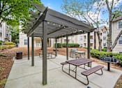 Thumbnail 12 of 29 - A picnic area with a canopy and benches is surrounded by apartment buildings.