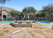Thumbnail 23 of 54 - A pool surrounded by a stone patio with a fountain in the middle.