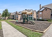 Thumbnail 25 of 54 - A playground with a green slide and a brown gravel area in front of a row of houses.