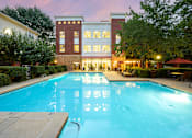 Thumbnail 3 of 80 - A large swimming pool in front of a building with a red umbrella and chairs around it.