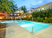 Thumbnail 4 of 80 - A large swimming pool surrounded by a concrete patio and residential buildings.