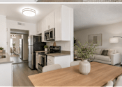 Thumbnail 8 of 15 - A modern kitchen with white cabinets and a wooden table.