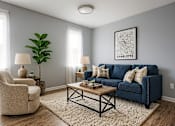 Thumbnail 30 of 35 - A living room with a blue couch, a chair, a coffee table, and a plant.