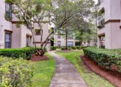 Thumbnail 6 of 20 - a sidewalk leading to an apartment building with trees and bushes at Stone Creek at Old Farm Apartments, Houston, 77063