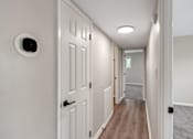 Thumbnail 2 of 12 - A hallway with a white door and a white wall with a round black device on it.
