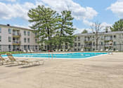 Thumbnail 6 of 14 - A pool surrounded by chairs and trees in front of apartment buildings.