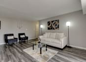 Thumbnail 3 of 11 - A living room with a white couch, a black chair, and a glass coffee table.