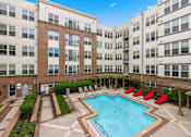 Thumbnail 4 of 57 - A large swimming pool surrounded by red chairs and apartment buildings.