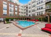 Thumbnail 39 of 57 - A swimming pool surrounded by red lounge chairs and apartment buildings.