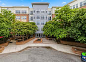 Thumbnail 45 of 57 - A car is parked on the right side of a courtyard with a building in the background.