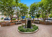 Thumbnail 36 of 57 - A park with a fountain surrounded by benches and trees.