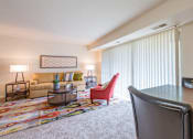 Thumbnail 5 of 18 - A living room with a red chair and a grey desk.