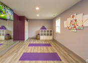 Thumbnail 32 of 33 - A yoga studio with purple mats and a flat screen TV mounted on the wall.