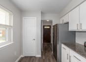 Thumbnail 16 of 29 - a kitchen with white cabinets and a door to a hallway with a refrigerator