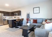 Thumbnail 2 of 17 - A modern kitchen with a grey couch and a black table.