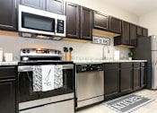 Thumbnail 12 of 17 - A kitchen with dark brown cabinets and stainless steel appliances.