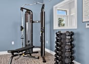 Thumbnail 10 of 16 - A gym room with a squat rack, bench, and a stack of dumbbells.
