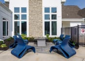 Thumbnail 13 of 37 - a patio with blue chairs and a fire pit in front of a building at The Edison at Blue Springs, Blue Springs, 64014