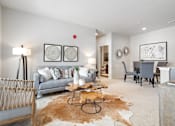 Thumbnail 8 of 23 - A living room with a grey couch, a brown cowhide rug, and a wooden coffee table.