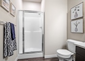 Thumbnail 3 of 16 - A bathroom with a toilet, a shower with a glass door, and towels hanging on a rack.