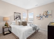 Thumbnail 33 of 41 - A bedroom with a large bed, a lamp, and two paintings on the wall at Aventura at Wentzville I & II Apartments, Wentzville, MO, 63385