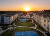 Thumbnail 23 of 37 - an aerial view of an apartment complex with a pool and tennis court at sunset at The Edison at Blue Springs, Blue Springs, 64014