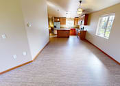 Thumbnail 27 of 28 - A large empty room with wooden floors and a kitchen area in the background.