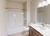Thumbnail 20 of 28 - A white bathroom with a toilet, sink, and a shower with a glass door.