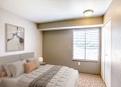 Thumbnail 6 of 18 - A bedroom with a bed, pillows, a nightstand, and a window with blinds.