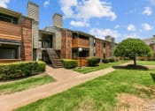 Thumbnail 35 of 50 - a grassy area with a tree and bushes in front of an apartment building at The Hills at Ironhorse, North Richland Hills