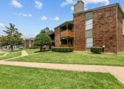 Thumbnail 38 of 50 - a grassy area with trees and bushes in front of a brick building at The Hills at Ironhorse, Texas