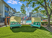 Thumbnail 8 of 15 - two lounge chairs with umbrellas in front of a pool at Peaks at Northwest Hills Apartments, Texas