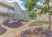 Thumbnail 27 of 68 - a patio with a stone wall and purple flowers in front of a building at The Escapade, San Antonio, Texas