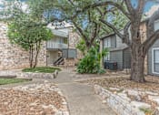 Thumbnail 34 of 68 - a walkway between two buildings with trees and rocks at The Escapade, San Antonio