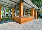 Thumbnail 22 of 26 - A wooden structure with a roof and pillars is situated on a brick path.