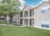 Thumbnail 10 of 12 - A beige two-story apartment building with a black fence and a green lawn.
