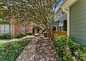 Thumbnail 11 of 20 - Courtyard walkway with mature trees and landscaping at Knoll Crest Apartments, San Antonio, TX