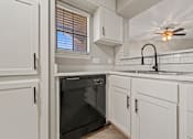 Thumbnail 16 of 38 - an empty kitchen with white cabinets and a black dishwasher at Polo Clubs Apartments, Austin, TX
