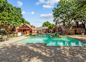 Thumbnail 4 of 32 - A large swimming pool surrounded by trees and a building in the background.