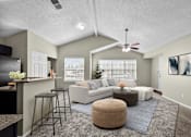 Thumbnail 19 of 32 - A living room with a white couch, a brown ottoman, and a ceiling fan.