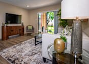 Thumbnail 2 of 10 - A living room with a white couch, a wooden cabinet, a grey armchair, a glass coffee table, and a large window.